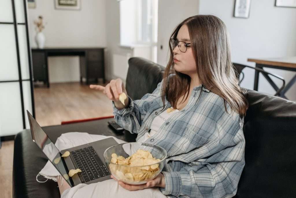 Woman Holding a Bowl of Potato Chips Sitting on a Couch 